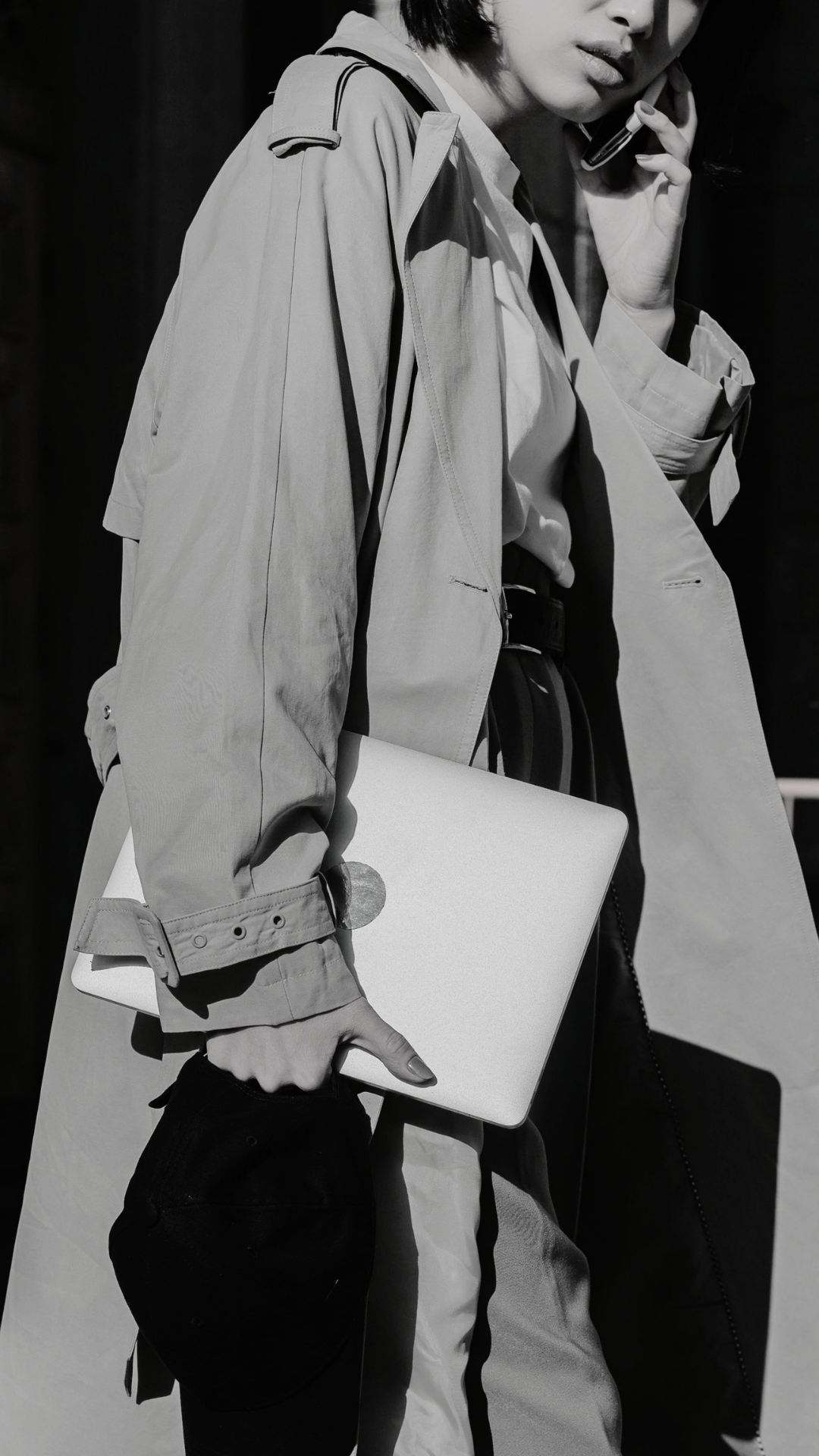 Woman in a trench coat on the phone carrying a laptop in the street underground private background intelligence