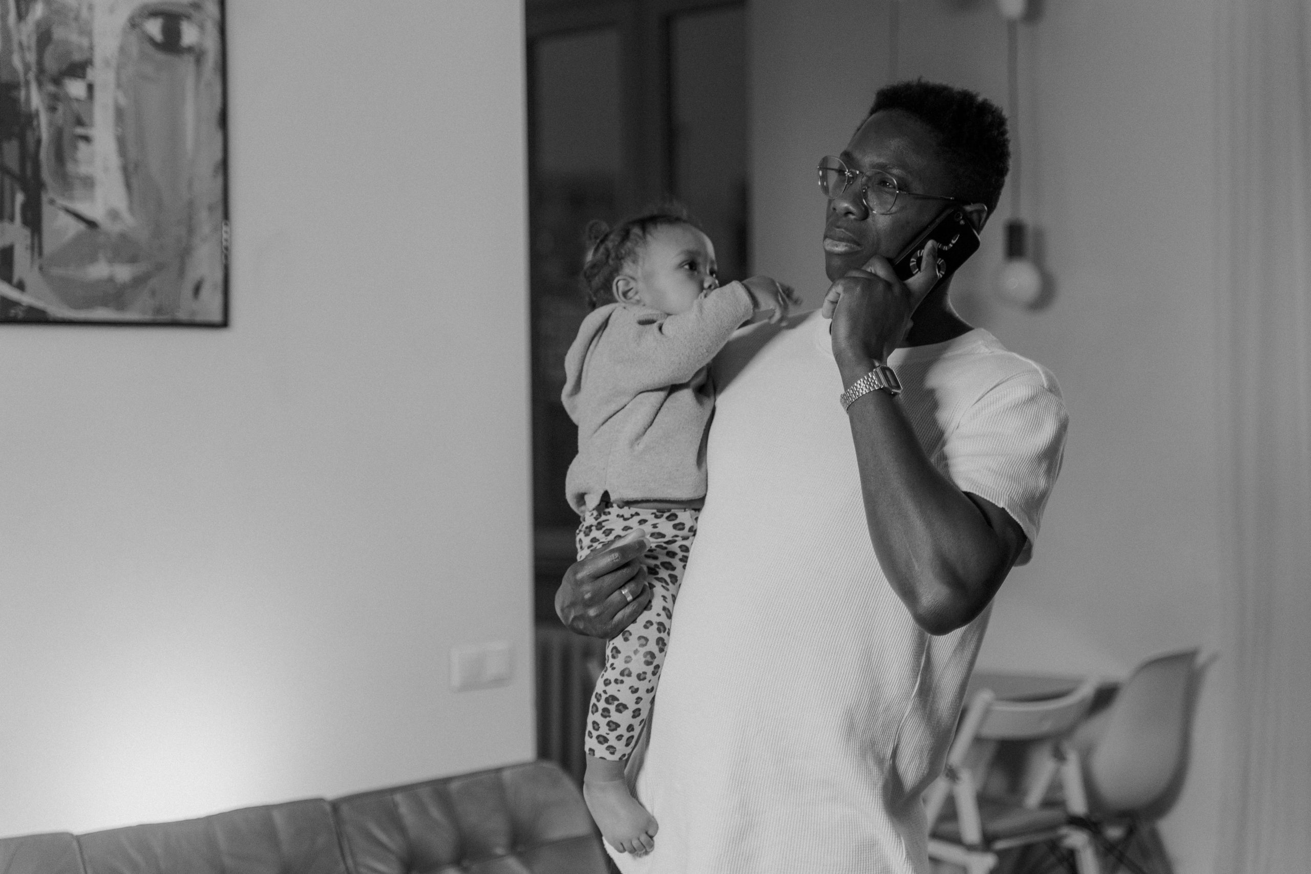 Parent holding a child at home while taking a phone call talking to Vera and Vale about domestic staff screening